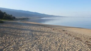A beach with a clear view of the ocean and distant mountains. - Appartement Neuf et son Jardin Pieds Dans le Sable (Saint Paul)