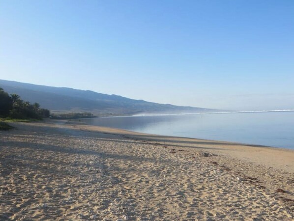 Una playa con vista clara al océano y montañas a lo lejos.