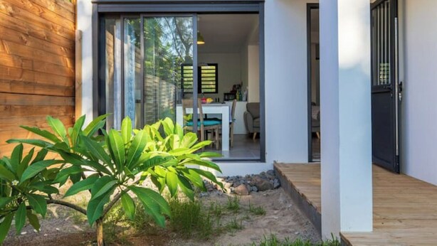 A modern house with a sliding glass door leading to a dining area. - Appartement Neuf et son Jardin Pieds Dans le Sable (Saint Paul)