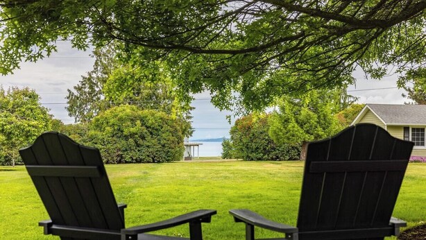 Due poltrone Adirondack rivolte verso un prato verde con vista su una casa e un corpo d'acqua.