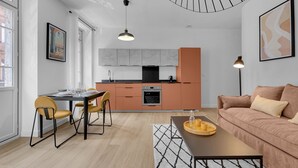 Une cuisine moderne avec un îlot central, un coin repas avec des chaises jaunes et un salon avec un canapé marron.