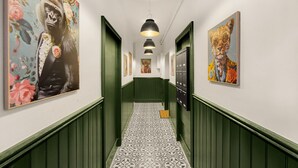 Un couloir aux murs verts, au sol recouvert de carreaux décoratifs et orné d’œuvres d’art représentant des animaux.
