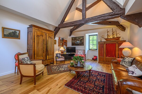 A spacious living room with wooden beams, a large wooden cabinet, a television, and a ship model on the wall.
