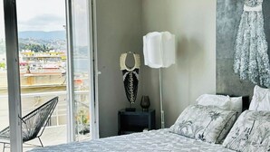 Ein Schlafzimmer mit einem großen Bett, einem Nachttisch, einer Lampe und Blick auf die Stadt durch eine Schiebetür.
