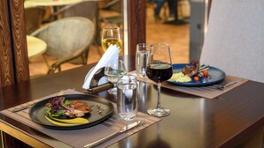 Una mesa de comedor con un plato de comida, un vaso de agua y una copa de vino tinto.