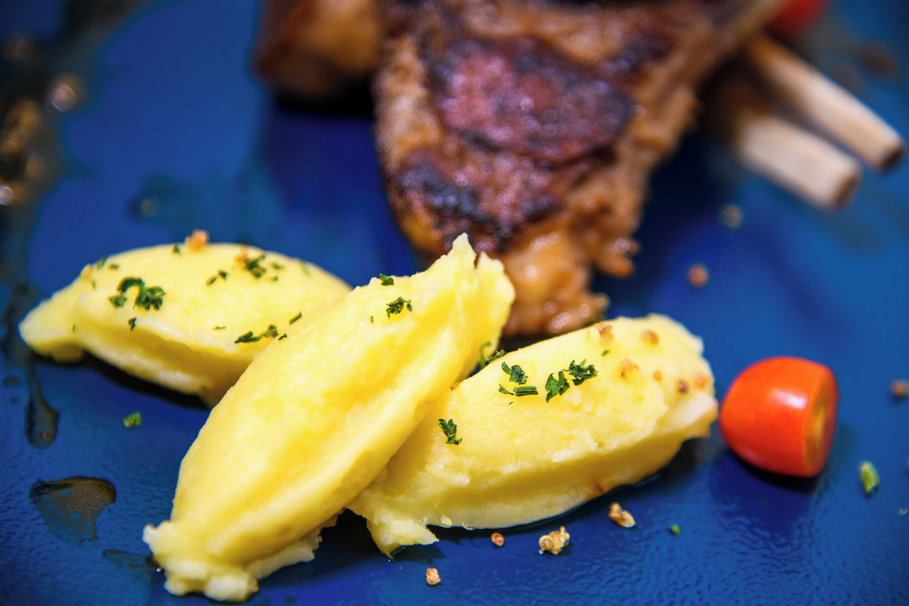 A steak with a side of mashed potatoes and a cherry tomato on a blue plate.