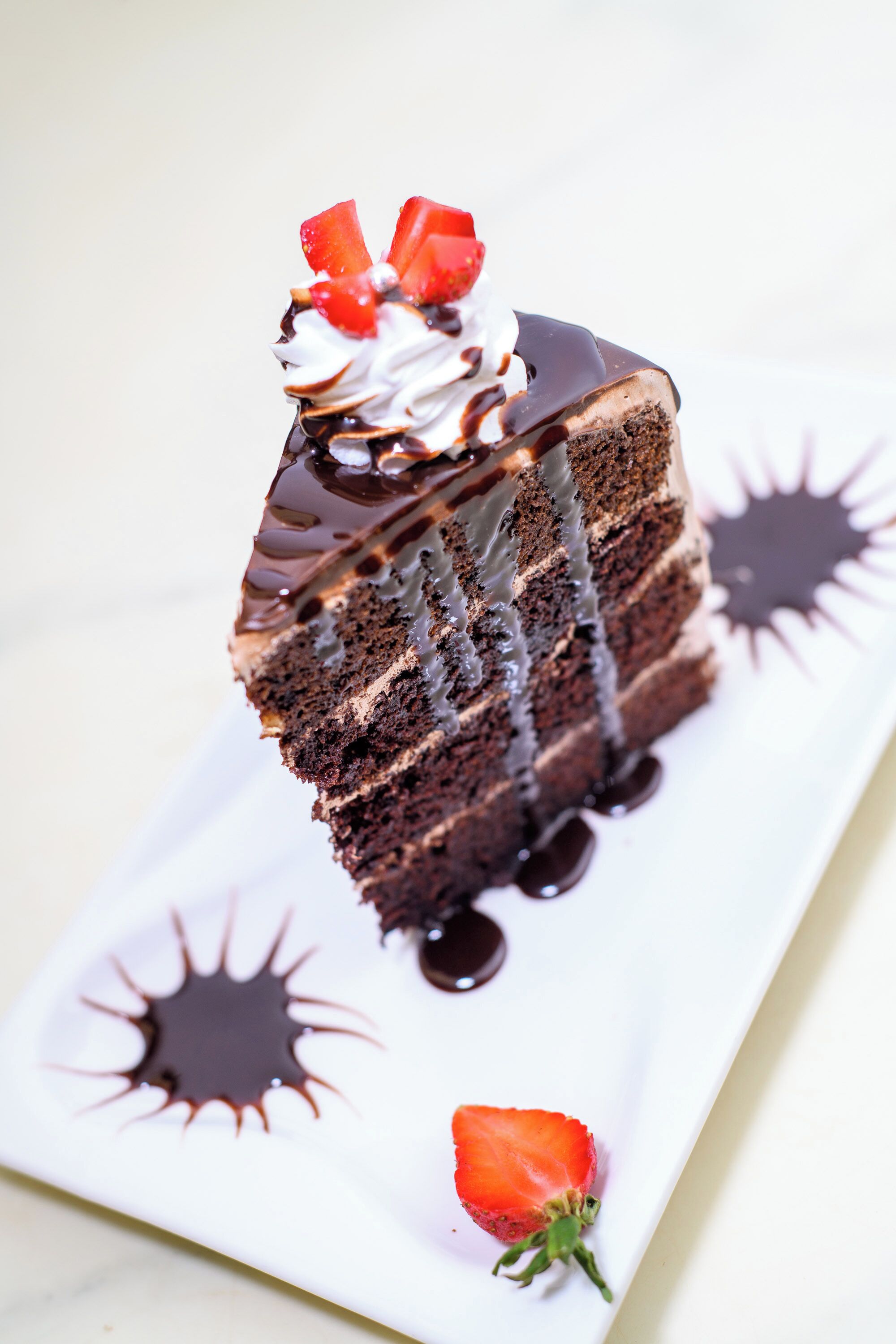 A slice of chocolate cake with strawberries and whipped cream on a white plate.