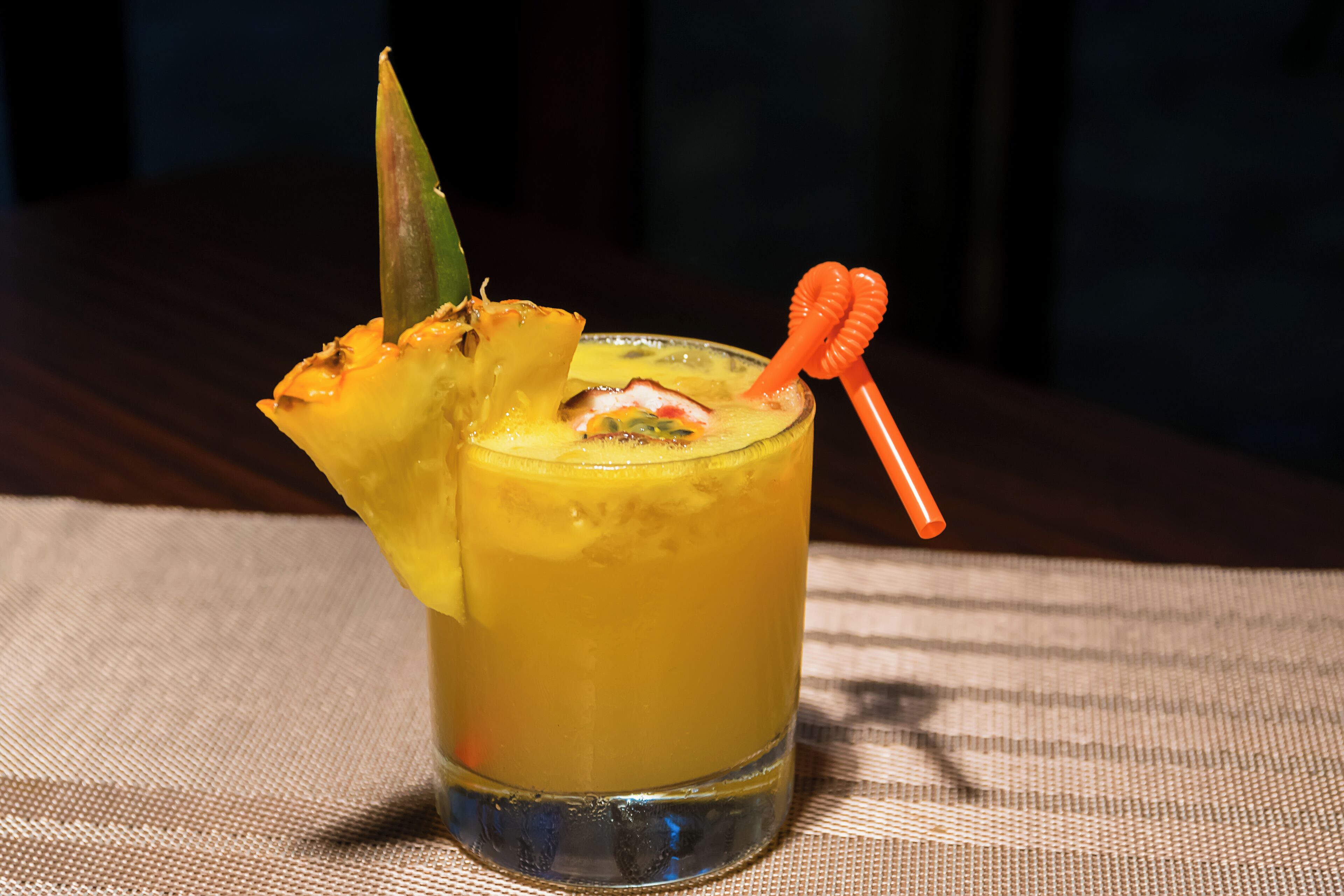 Un verre d’une boisson jaune, garni d’une tranche d’ananas et d’une paille orange décorative.