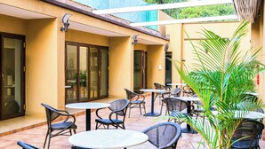 Un patio al aire libre con varias mesas y sillas redondas, rodeado de puertas y paredes de vidrio.