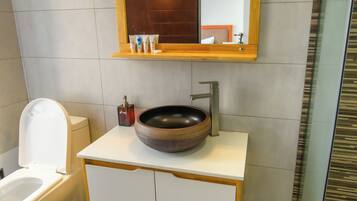 Ein Badezimmer mit einer weißen Toilette, einem runden Waschbecken mit Holzablage und einem Spiegel darüber.