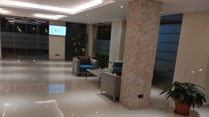 Un vestíbulo amplio con mostrador de recepción, zona de estar y una pantalla grande que muestra información.