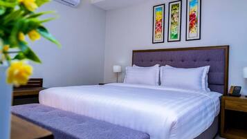 Ein Hotelzimmer mit einem großen Bett, einem Nachttisch, einer Bank und drei gerahmten Bildern an der Wand.