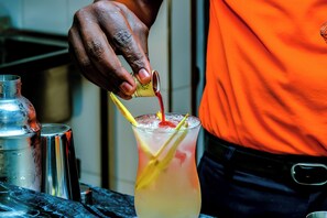 A person pouring a red liquid into a glass with a yellow straw and lemon slice. - Canary Hotel (Kampala)