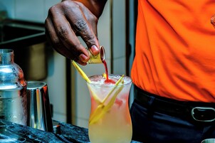 Una persona vertiendo un líquido rojo en un vaso con pajita amarilla y una rodaja de limón.