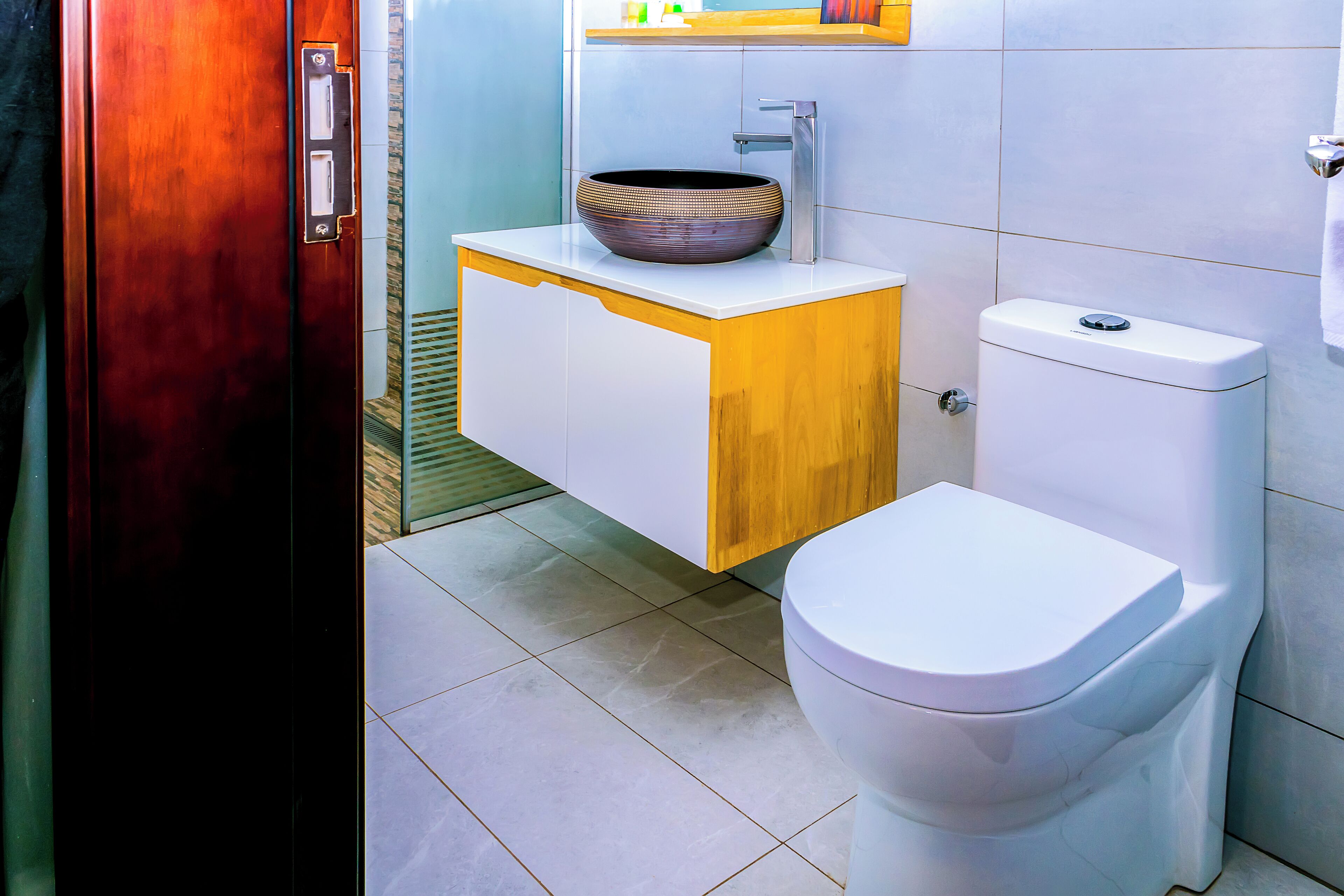 A bathroom with a white toilet, a wooden vanity with a vessel sink, and a tiled floor.