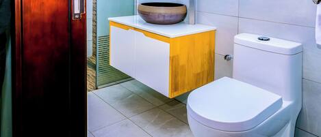 A bathroom with a white toilet, a wooden vanity with a vessel sink, and a tiled floor.
