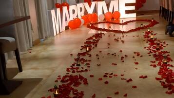 Decoración para una boda con un cartel que dice 'MARRY ME', globos rojos y pétalos de rosa en el suelo.