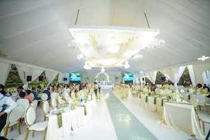 A tented event space with round tables, chairs, and a stage.