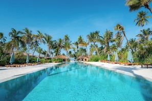 Une piscine d’un bleu éclatant, entourée de palmiers et de chaises longues en bois.