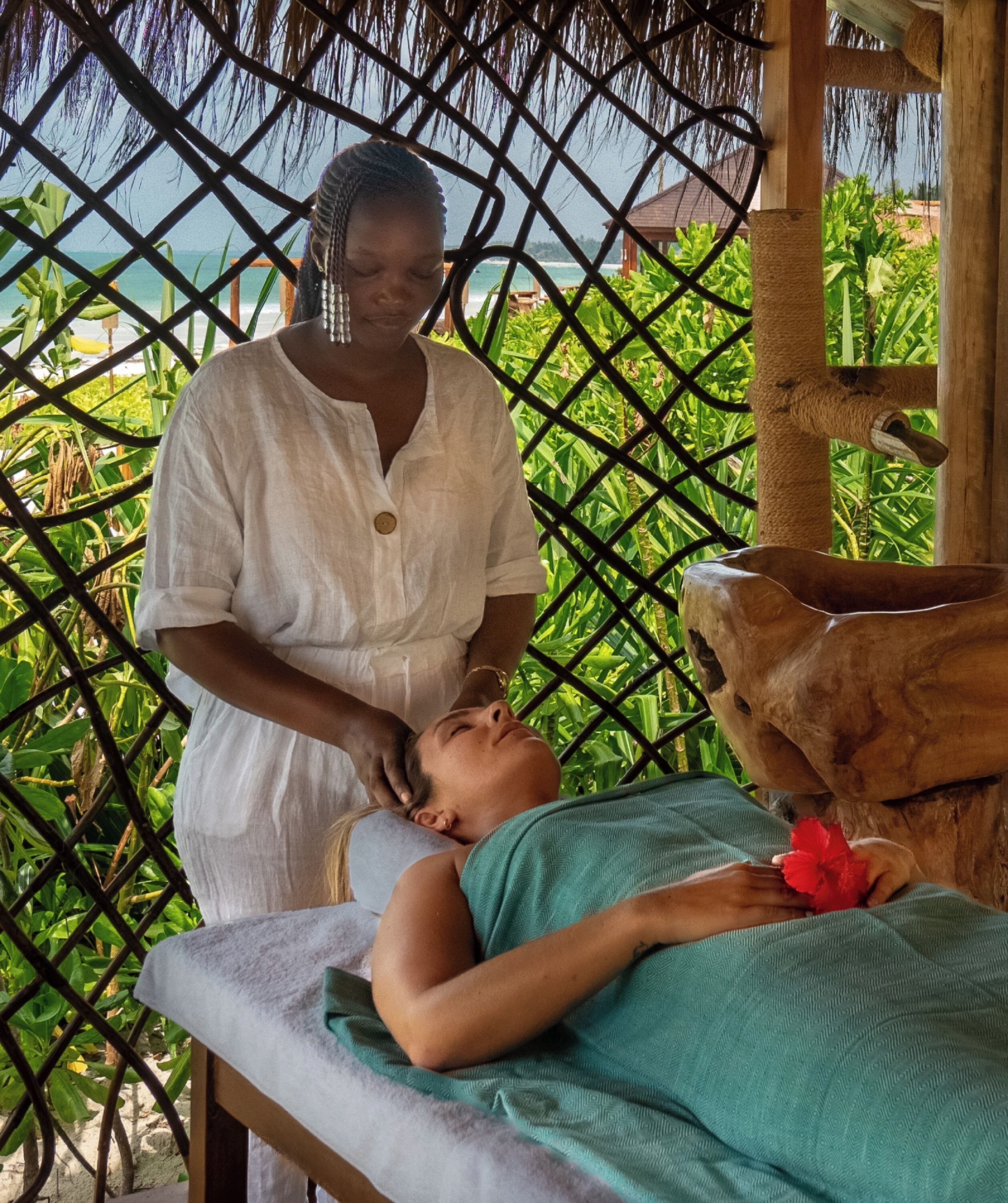 A person receiving a massage in a room with a wooden bench and a thatched roof.