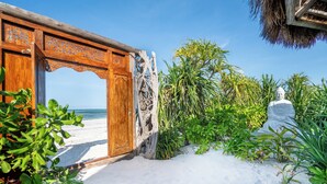 A wooden gate leading to a beach, surrounded by lush greenery and a Buddha statue. - Sensations Eco-Chic Hotel (Pwani Mchangani)