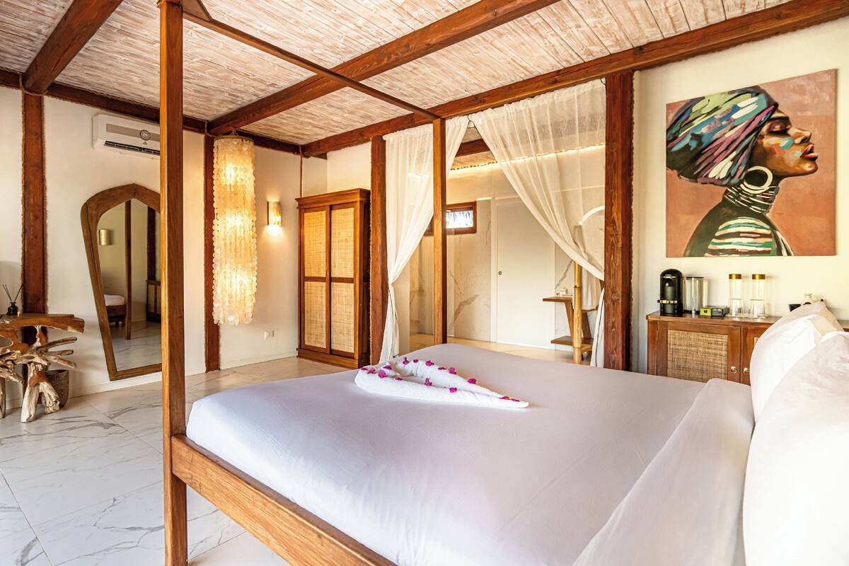 Un dormitorio con una cama grande, vigas de madera, un espejo, un cuadro y una mesita de noche con una lámpara.