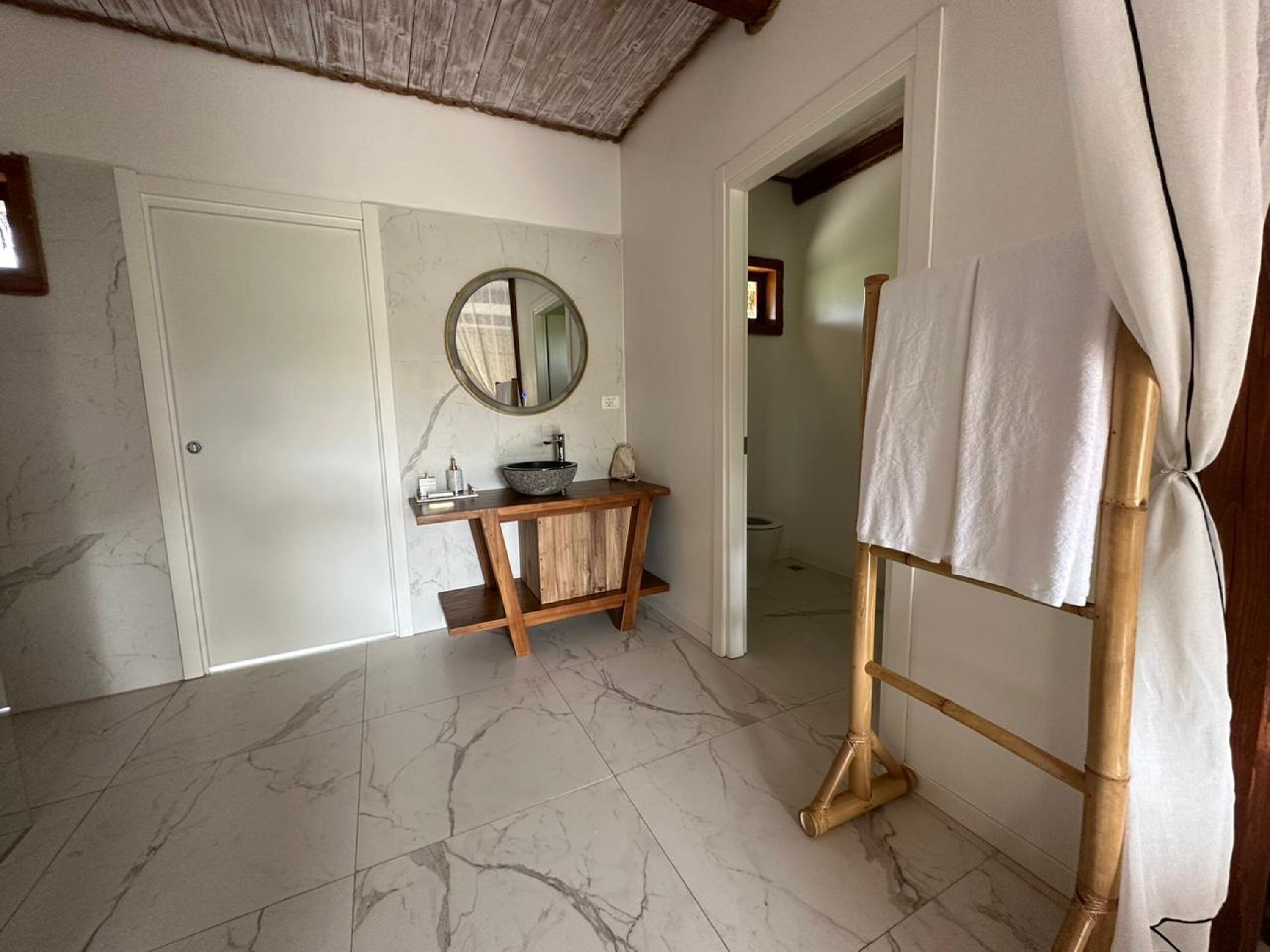 Une salle de bain avec un sol en marbre, un meuble-lavabo en bois, un miroir rond et un porte-serviettes.