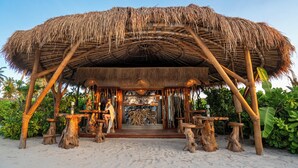 A thatched-roof structure with wooden tables and benches, surrounded by tropical plants. - Sensations Eco-Chic Hotel (Pwani Mchangani)