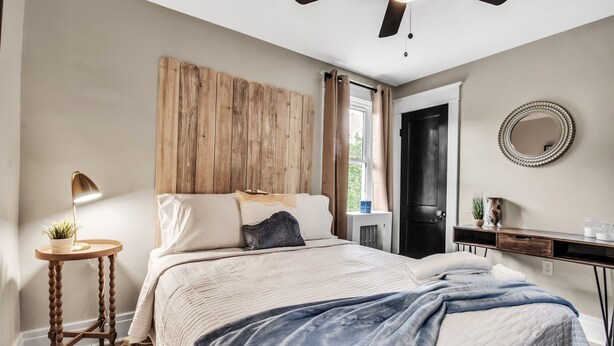 A bedroom with a bed, wooden headboard, bedside table with a lamp, and a dresser. - Chic Two Bedroom near Buffalo (Buffalo)