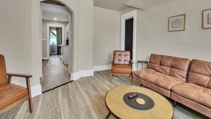 A spacious living room with a brown leather sofa, a round coffee table, and a brown leather armchair. A kitchen is visible in the background. - Chic Two Bedroom near Buffalo (Buffalo)