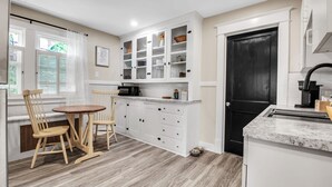 A kitchen with white cabinets, a black door, and a dining area with wooden chairs and a round table. - Chic Two Bedroom near Buffalo (Buffalo)