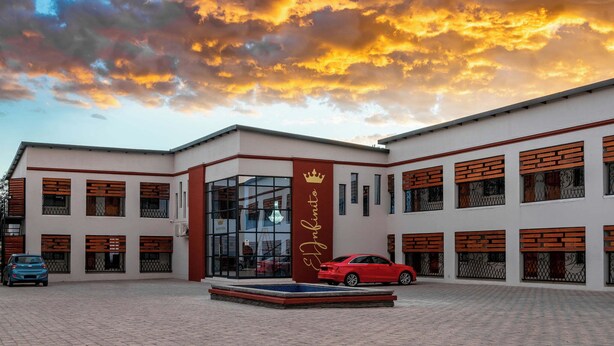 Un hotel con recepción, un coche rojo estacionado en la entrada y un amplio ventanal de vidrio.