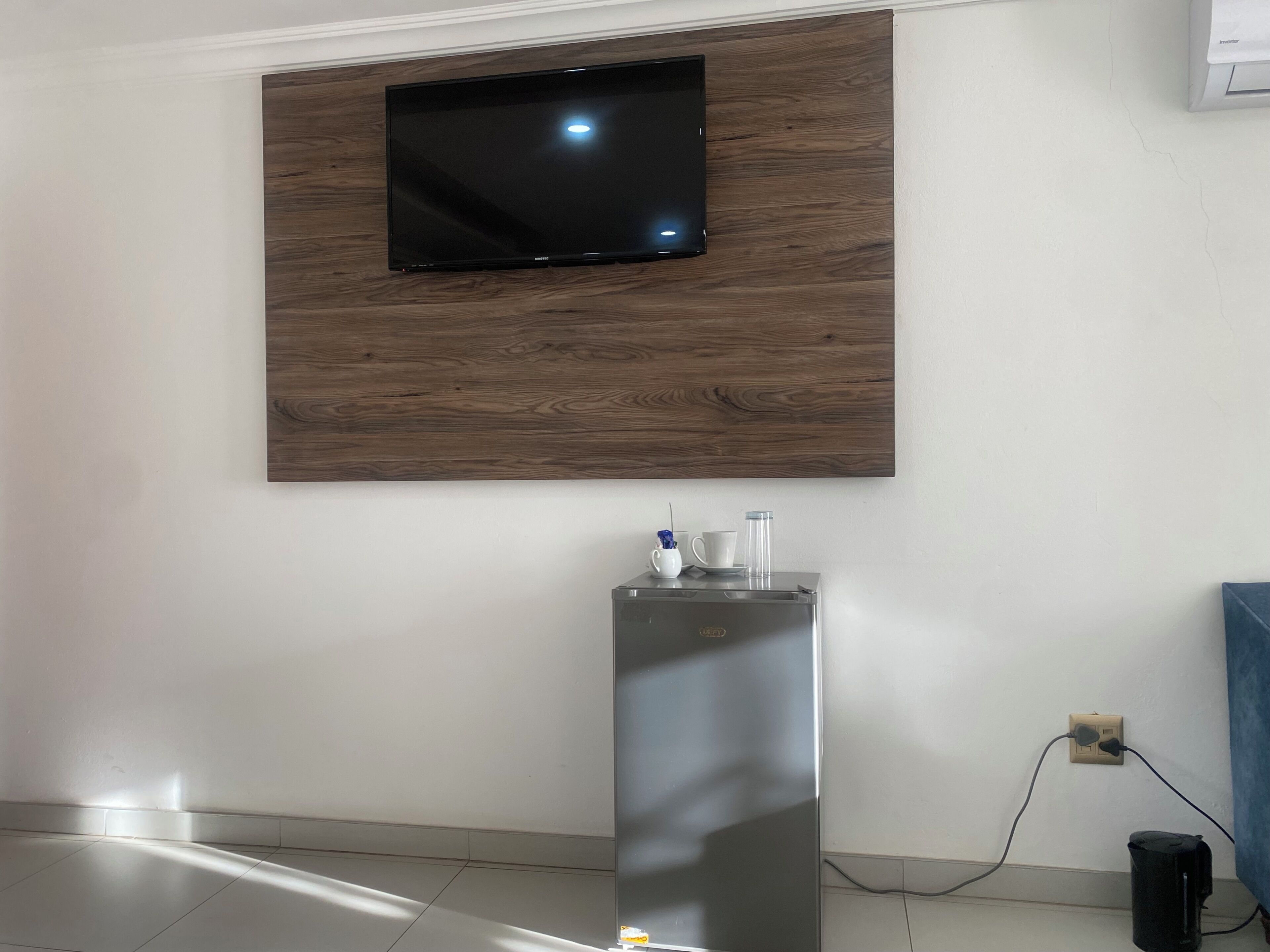 A modern room with a mounted TV, a metallic water dispenser, and a power outlet on the wall.