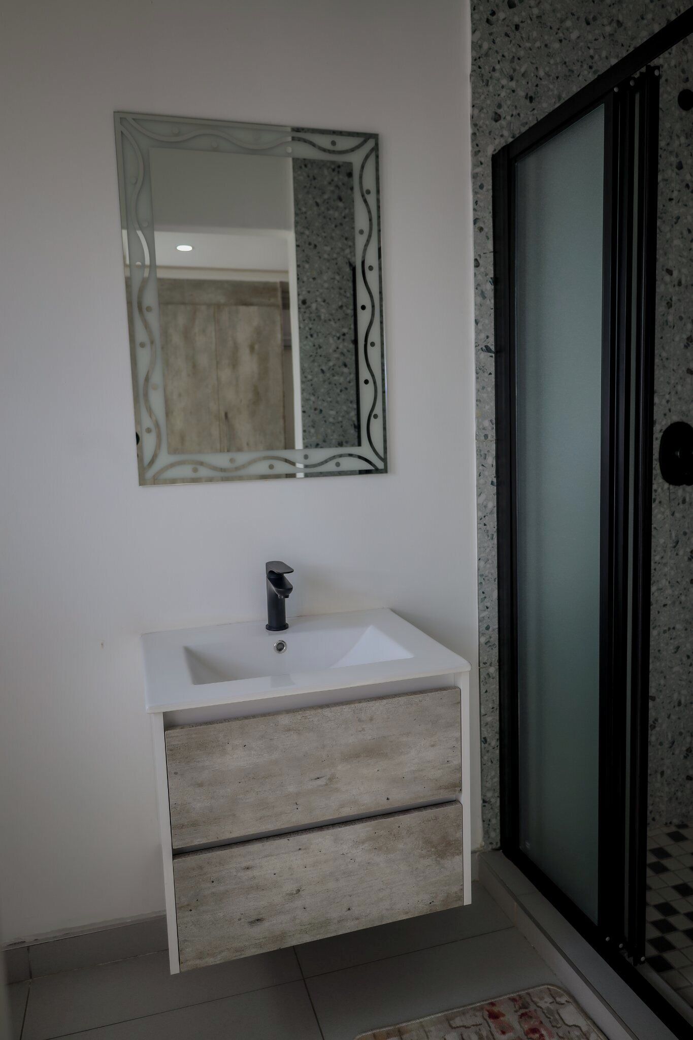Un baño con lavamanos blanco, un espejo con marco decorativo y una zona de ducha con puertas de vidrio esmerilado.