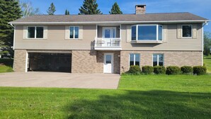 A two-story house with a garage, a balcony, and a well-maintained lawn. - Spacious, pet-friendly home in Hancock Twp. Includes indoor sauna! (Hancock)