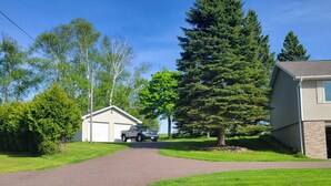 A residential driveway leading to a house with a garage, surrounded by trees and a well-maintained lawn. - Spacious, pet-friendly home in Hancock Twp. Includes indoor sauna! (Hancock)