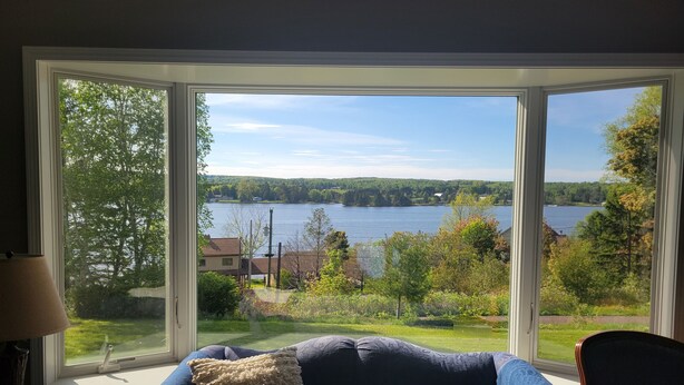 A room with a large window offering a view of a lake and surrounding greenery. - Spacious, pet-friendly home in Hancock Twp. Includes indoor sauna! (Hancock)