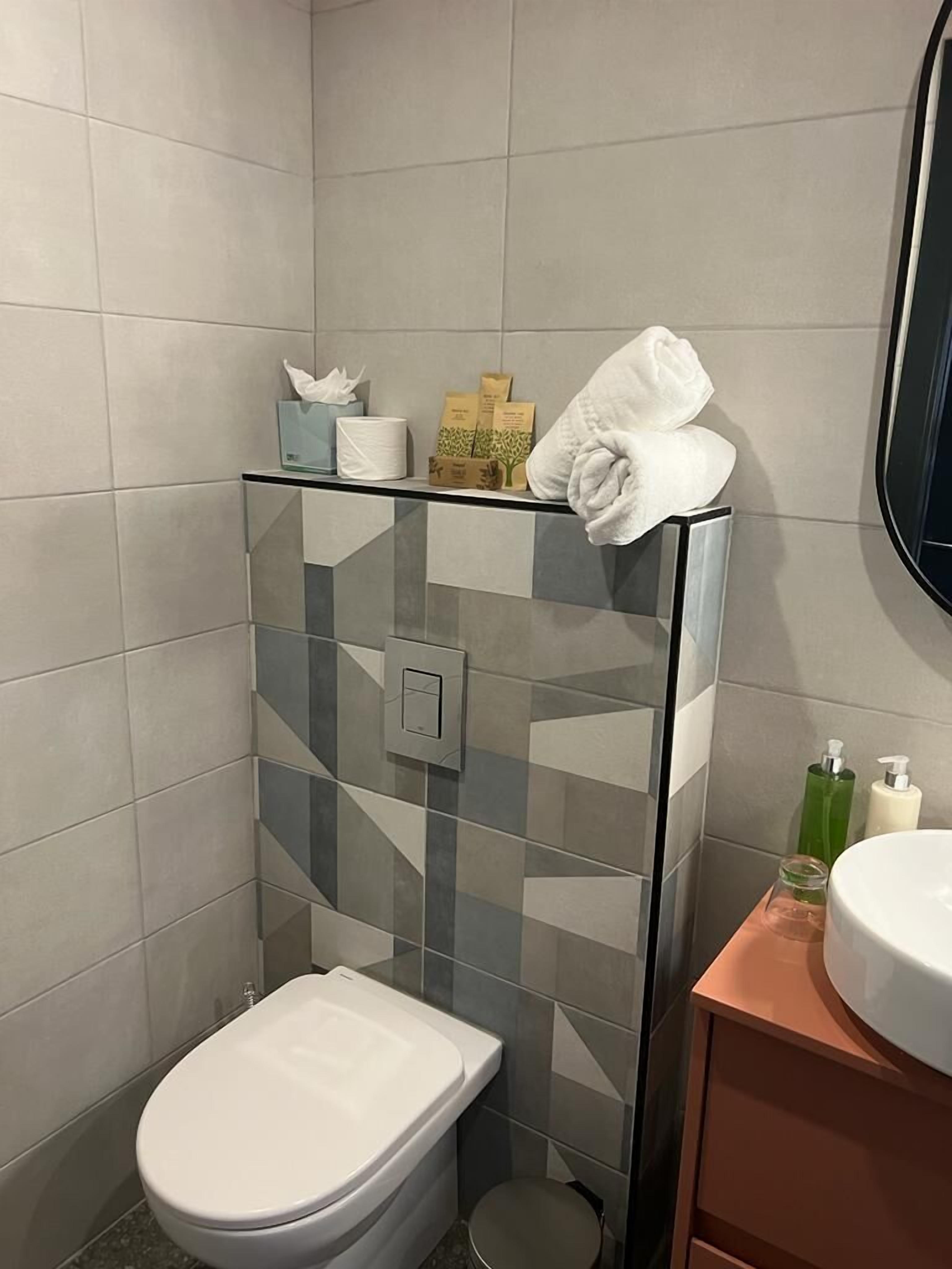 Ein modernes Badezimmer mit Duschkabine aus Glas, Toilette und Waschbecken mit Pflegeprodukten.