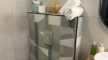 Ein modernes Badezimmer mit Duschkabine aus Glas, Toilette und Waschbecken mit Pflegeprodukten.