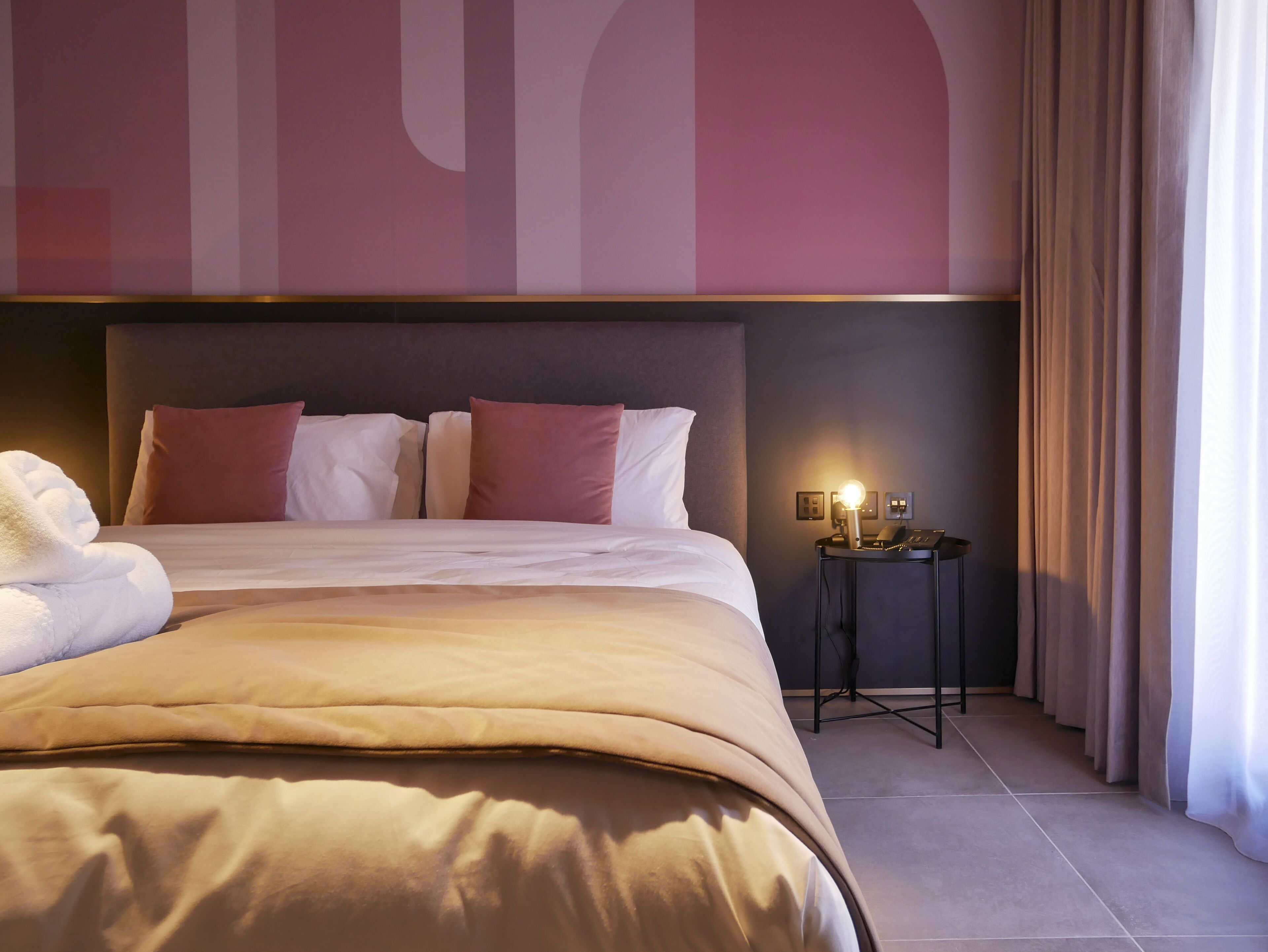 Una habitación de hotel con una cama grande, una mesita de noche con lámpara y una pared decorada con arte abstracto.
