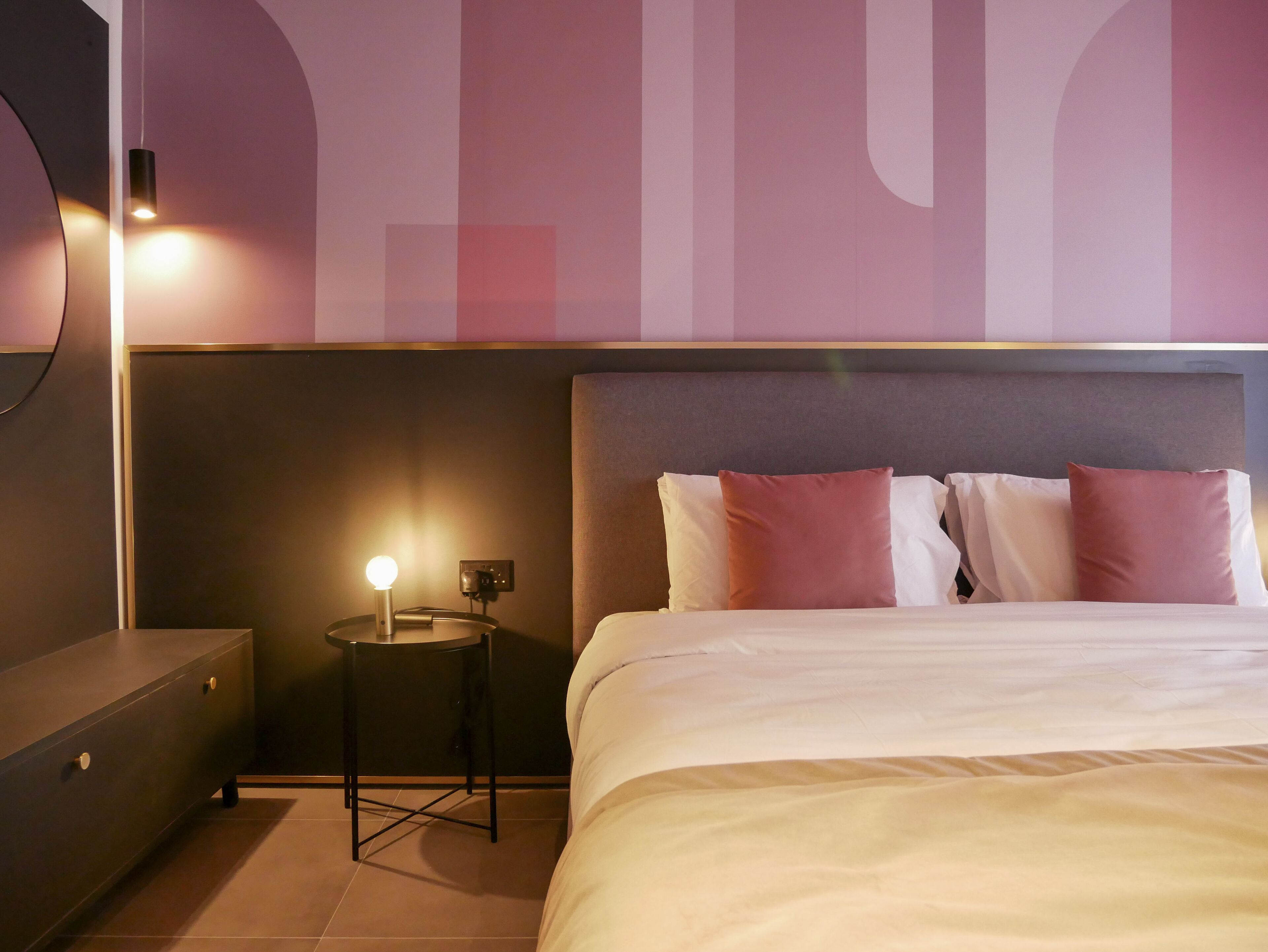 Habitación de hotel moderna con una cama grande, una mesita de noche con lámpara y un televisor montado en la pared.
