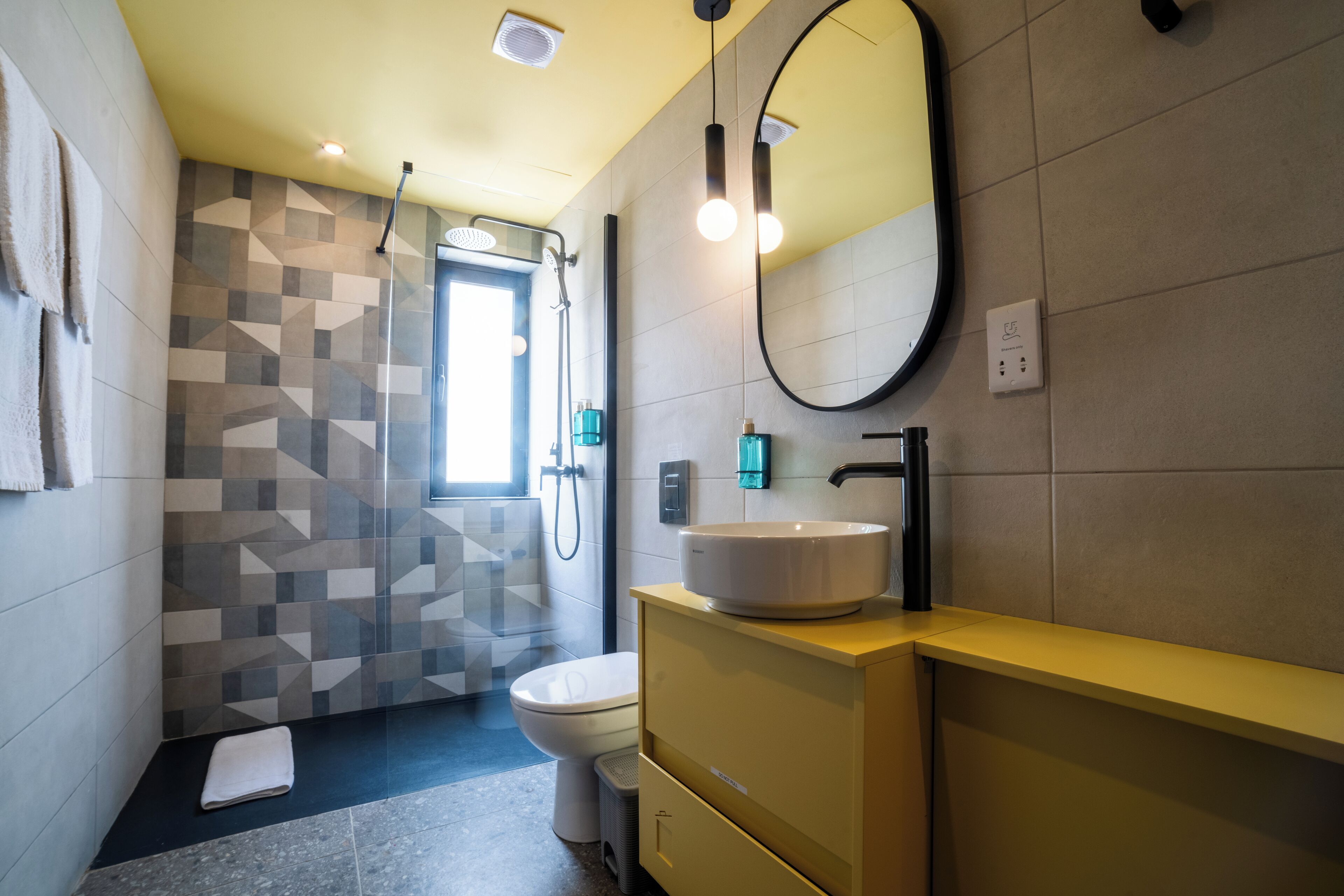 Uma casa de banho moderna com painel de azulejos geométricos, sanita, lavatório com espelho e zona de duche.