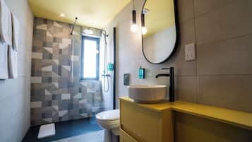 Uma casa de banho moderna com painel de azulejos geométricos, sanita, lavatório com espelho e zona de duche.