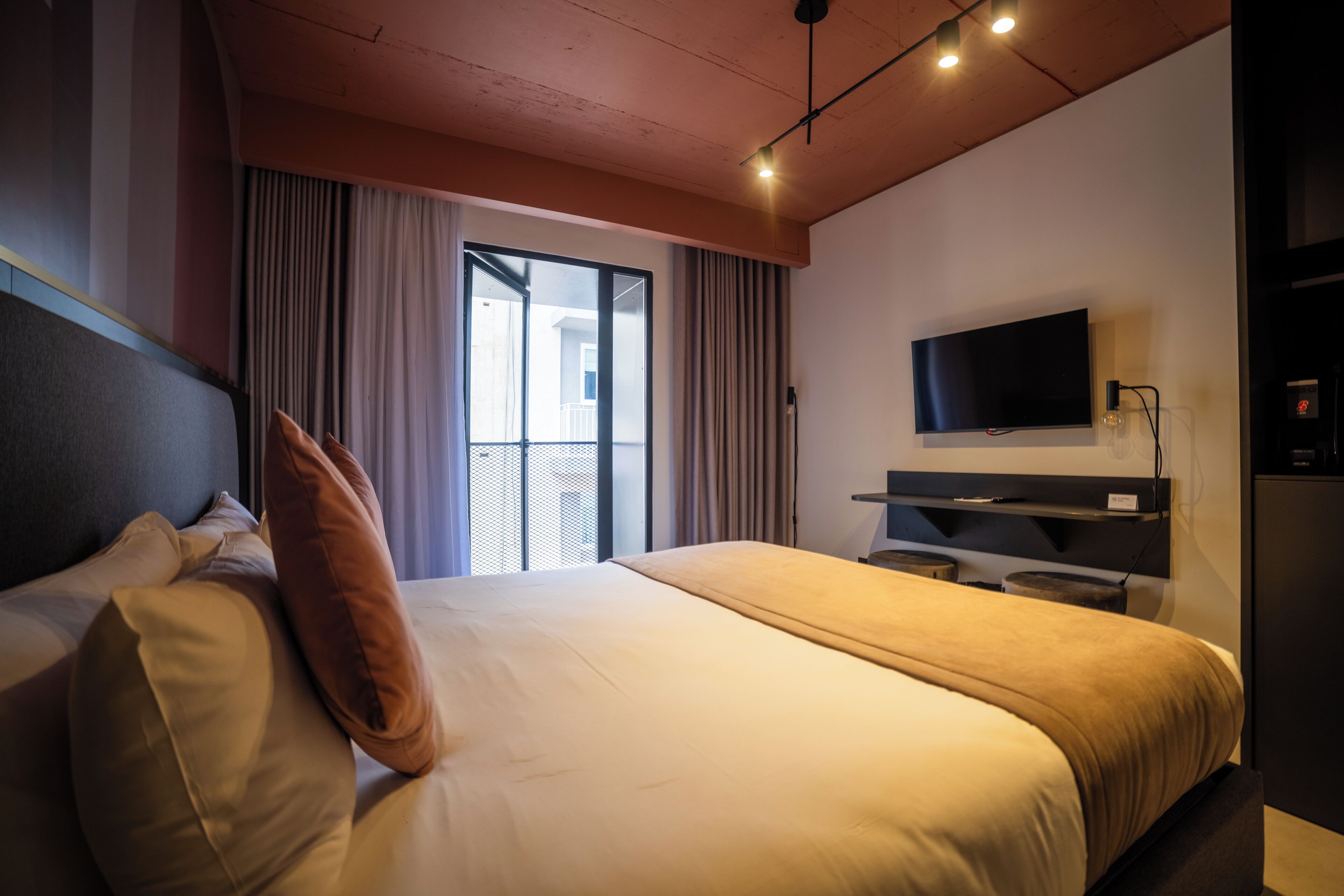 Ein Hotelzimmer mit einem großen Bett, einem flachbildfernseher an der Wand und einer Schiebetür zu einem Balkon.