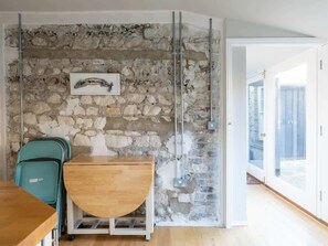 A room with a stone wall, a wooden table, a teal chair, and a window with a view.