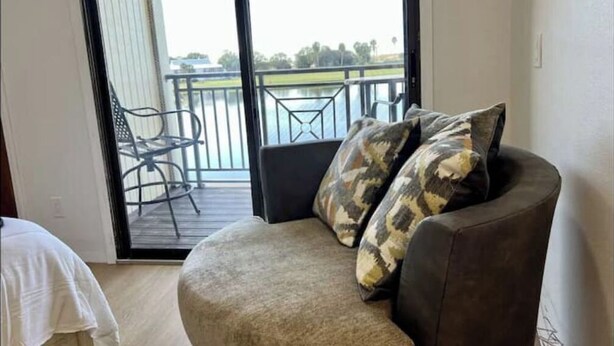 A balcony with a view of a body of water and trees, a chair, and a sofa with patterned cushions.