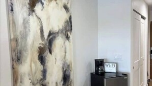 A room with a large abstract painting on the wall, a black coffee maker on a side table, and a sign indicating Wi-Fi availability.