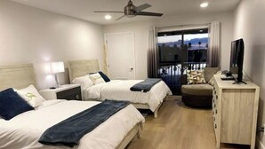 A hotel room with two beds, a TV, a desk, and a balcony with a view.