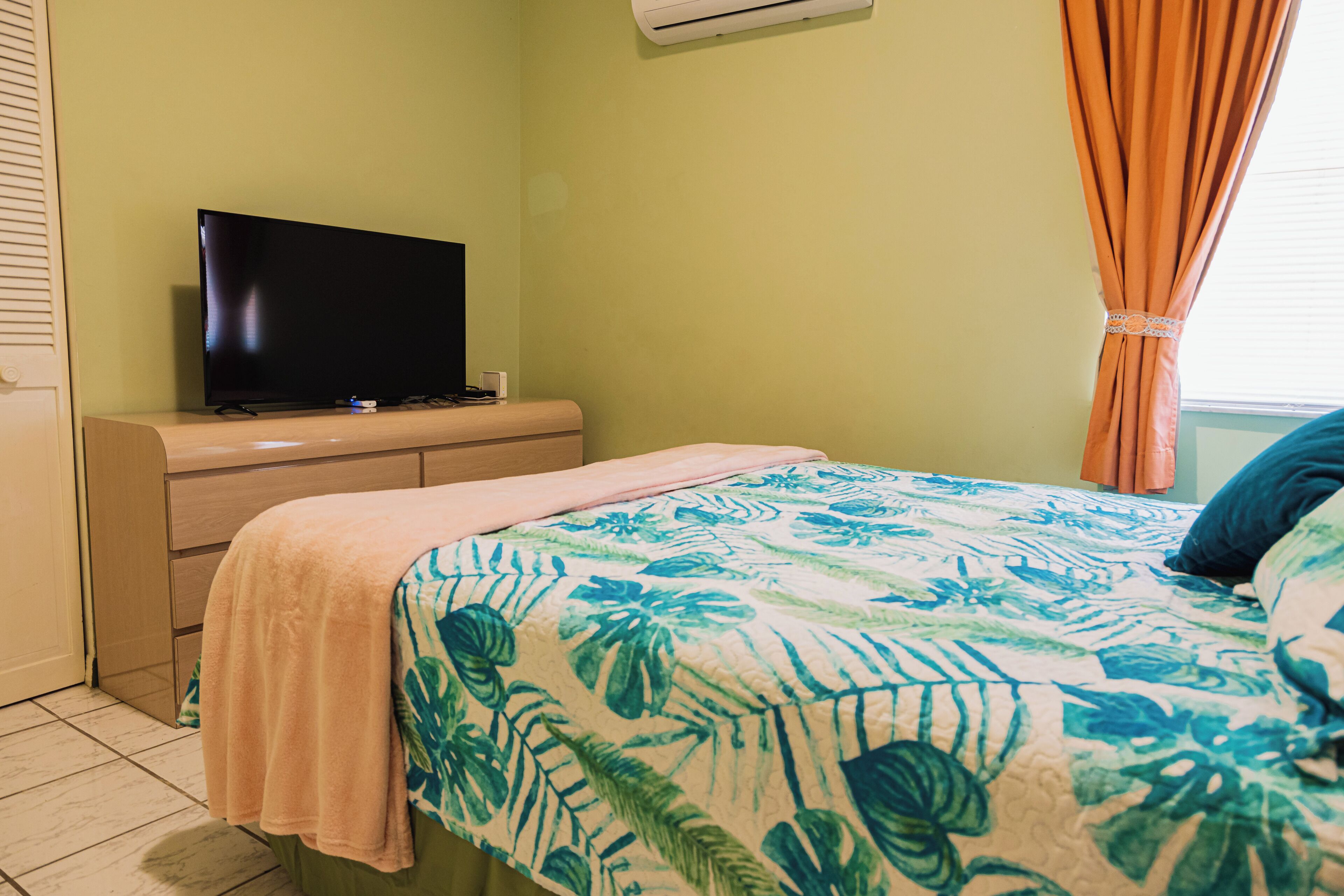A bedroom with a bed, a television on a dresser, and a window with curtains.