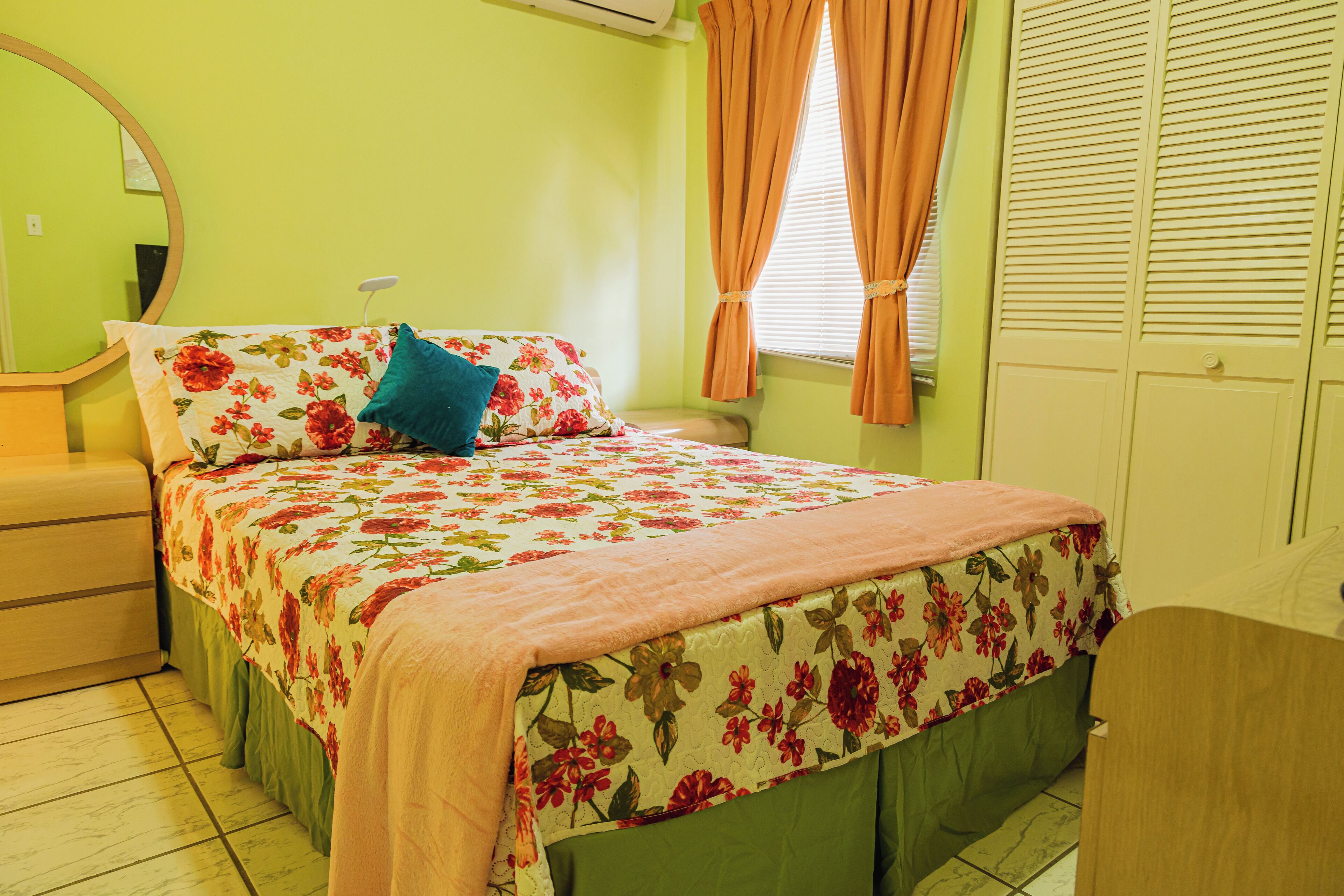 A bedroom with a floral bedspread, a green wall, and a wooden dresser.